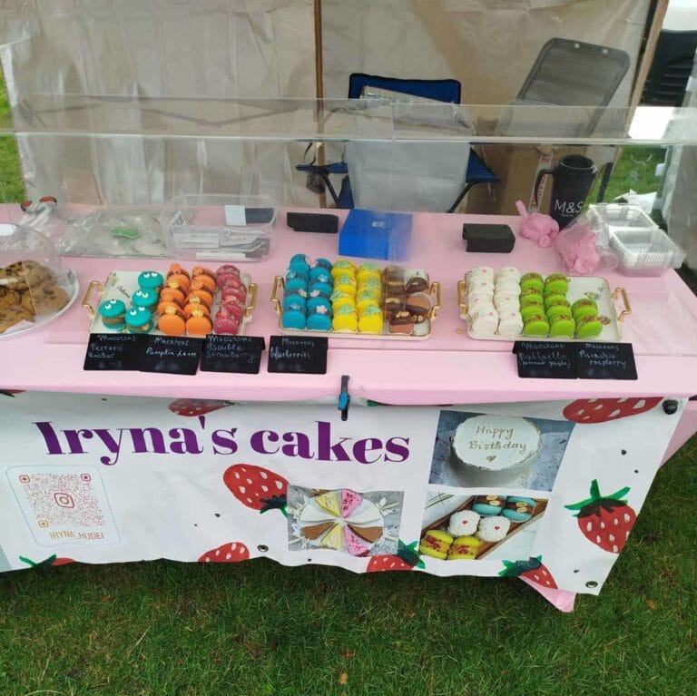 A market stall table at Portobello Market in Edinburgh displays colorful macarons and pastries under an Irynas Cakes sign with strawberries.