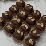 Rows of chocolate-covered mini cakes, topped with peanut halves, arranged neatly on a white marble surface—perfect for your next Elementor project.