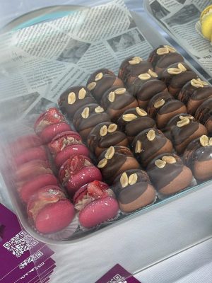 A tray of assorted macarons, made with Elementor flair, features pink with nuts and chocolate-covered with peanuts on newspaper-lined glass.