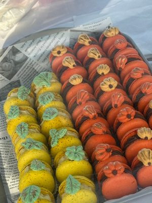 Rows of yellow and orange macarons, styled with flower-shaped decor, bring an Elementor-inspired elegance to a tray lined with newspaper.