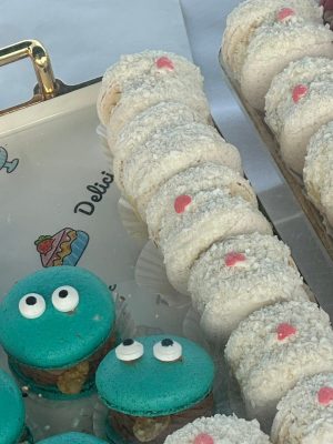 A tray with teal Elementor-themed macarons decorated with candy eyes and white macarons topped with pink heart-shaped decorations.