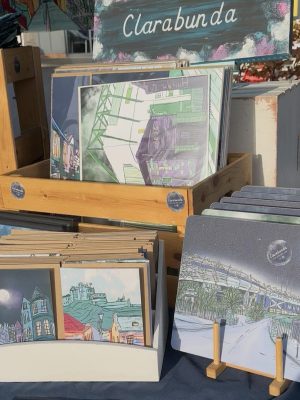 Display stand of illustrated postcards and prints with urban and nighttime scenes at Roswell Market, labeled Clarabunda at the top.
